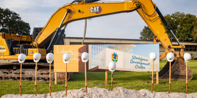 Picture of shovels in the ground with hard hats on them in front of a sign that says Workforce Development Center and a large piece of construction equipment