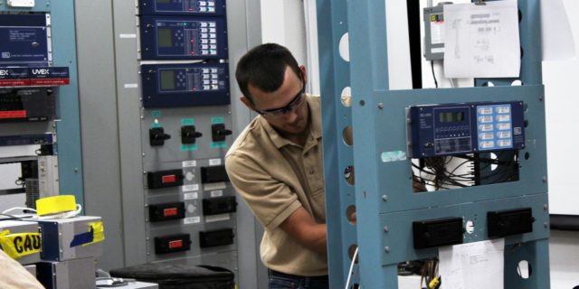 Man in khaki colored polo working on a free-standing protective relay equipment