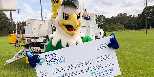 Swoop the Lakehawk holding an oversized $120,000 check from Duke Energy with a utility truck in the background