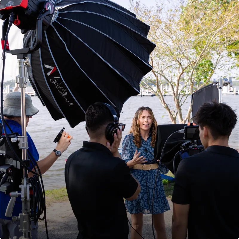 Person being interviewed by a film crew outdoors near a body of water.